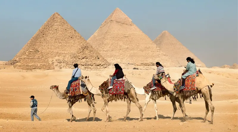 Tourists on a camel caravan riding past the Pyramids of Giza